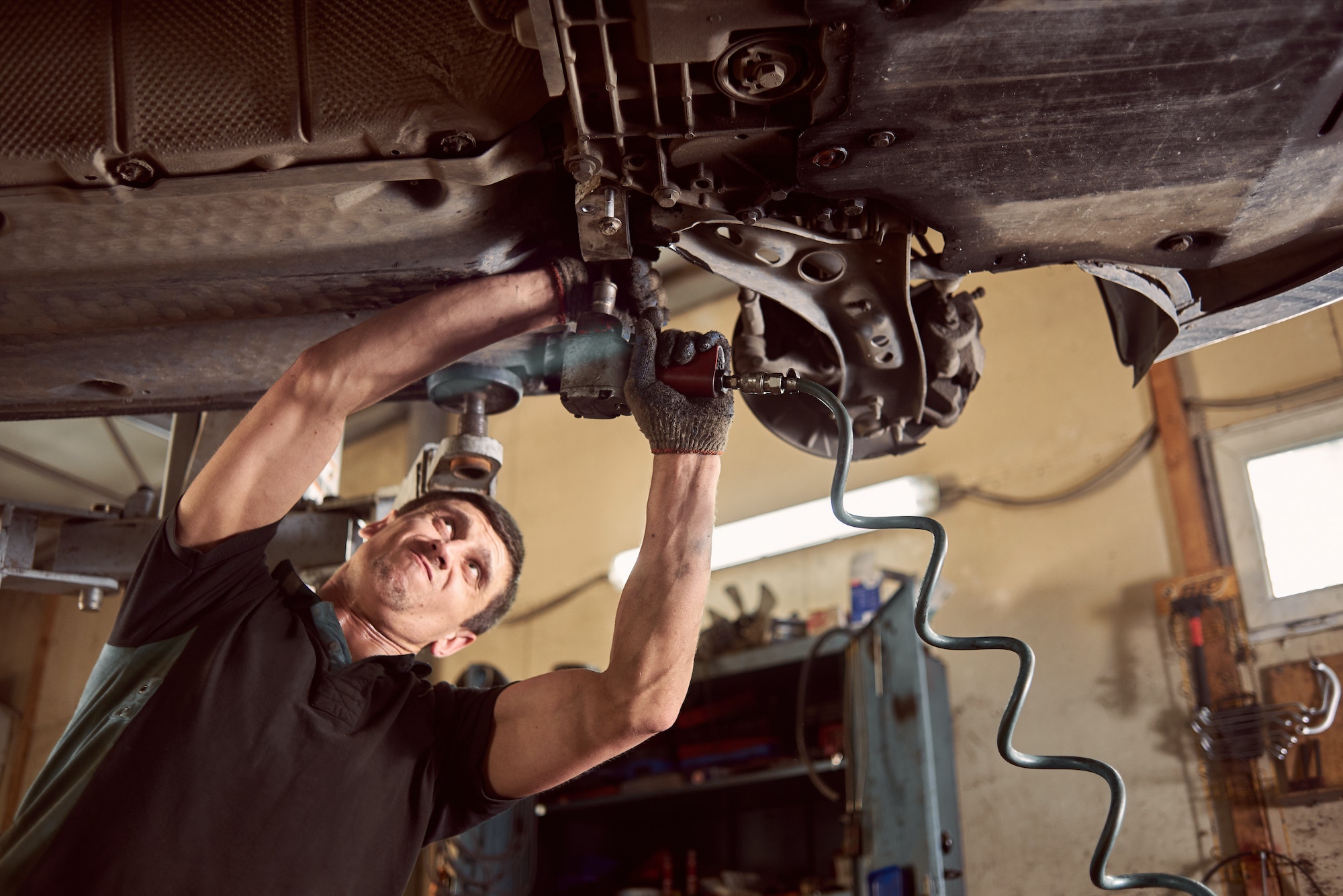 Repair man fixing car in repair station under lifted car during repair in garage