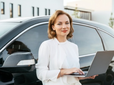 Smiling manager using laptop standing near new car. Dealership, car rental concept