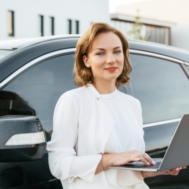 Smiling manager using laptop standing near new car. Dealership, car rental concept