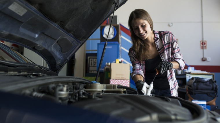 Young casual woman in shirt and gloves working with car in repair service checking engine oil level